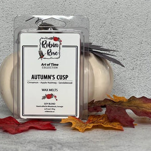 Wax Melt Clamshell standing up in front of a pumpkin with fall leaves. Container label has a robin and a rose on i