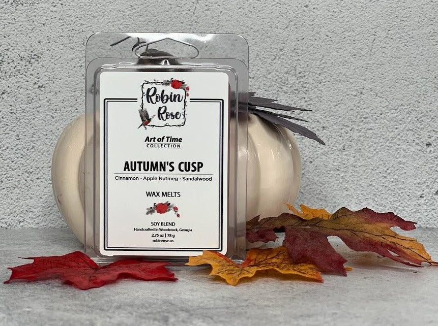 Wax Melt Clamshell standing up in front of a pumpkin with fall leaves. Container label has a robin and a rose on i