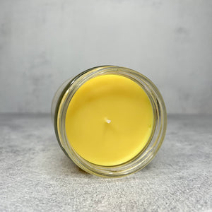 Container candle with yellow wax laying on its side showing inside of jar and wick