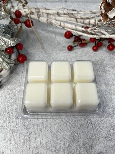 Picture of 6 wax melt cubes laying upside down featuring the white cubes. Container is laying beside Christmas tree and berries
