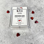 Wax melts in a clamshell container laying beside glass red hearts. Crushing gaze wax melts has a white label with robin and a rose on it