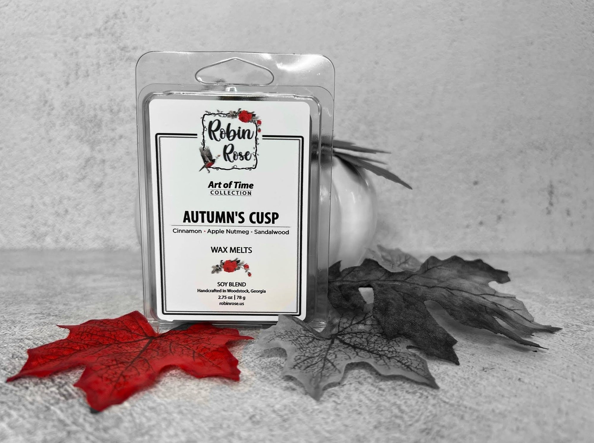 Wax Melt Clamshell standing up in front of a pumpkin with fall leaves. Container label has a robin and a rose on it.