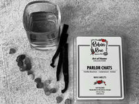 Shot of bourbon next to the vanilla sticks. Container of wax melts with a label with a robin and a rose on it
